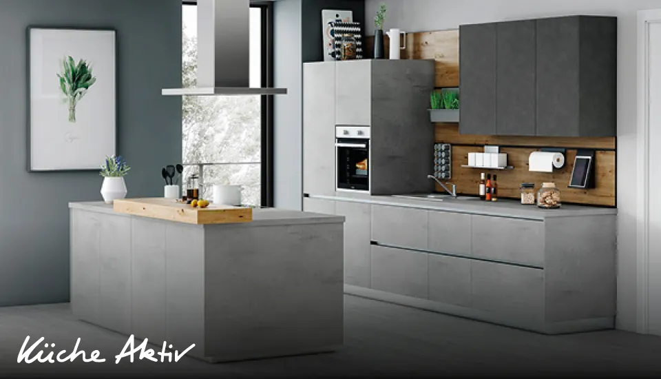 Moderne Küche in grauer Betonoptik mit Insel, Hängeschränken und Holzrückwand, ausgestattet mit Backofen, Dunstabzugshaube und dekorativen Accessoires vor großem Fenster